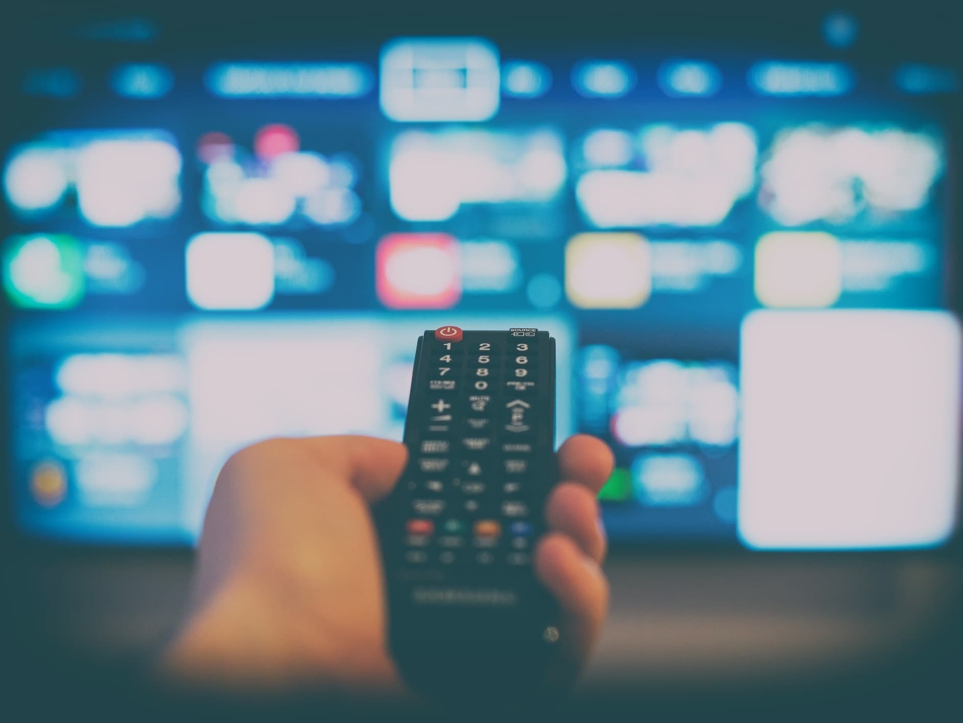 Pessoa navegando pelo menu de aplicativos de streaming usando o controle remoto da TV
